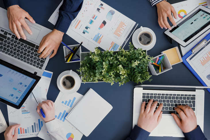 Mesa de trabajo con laptops, gráficos y equipo colaborando